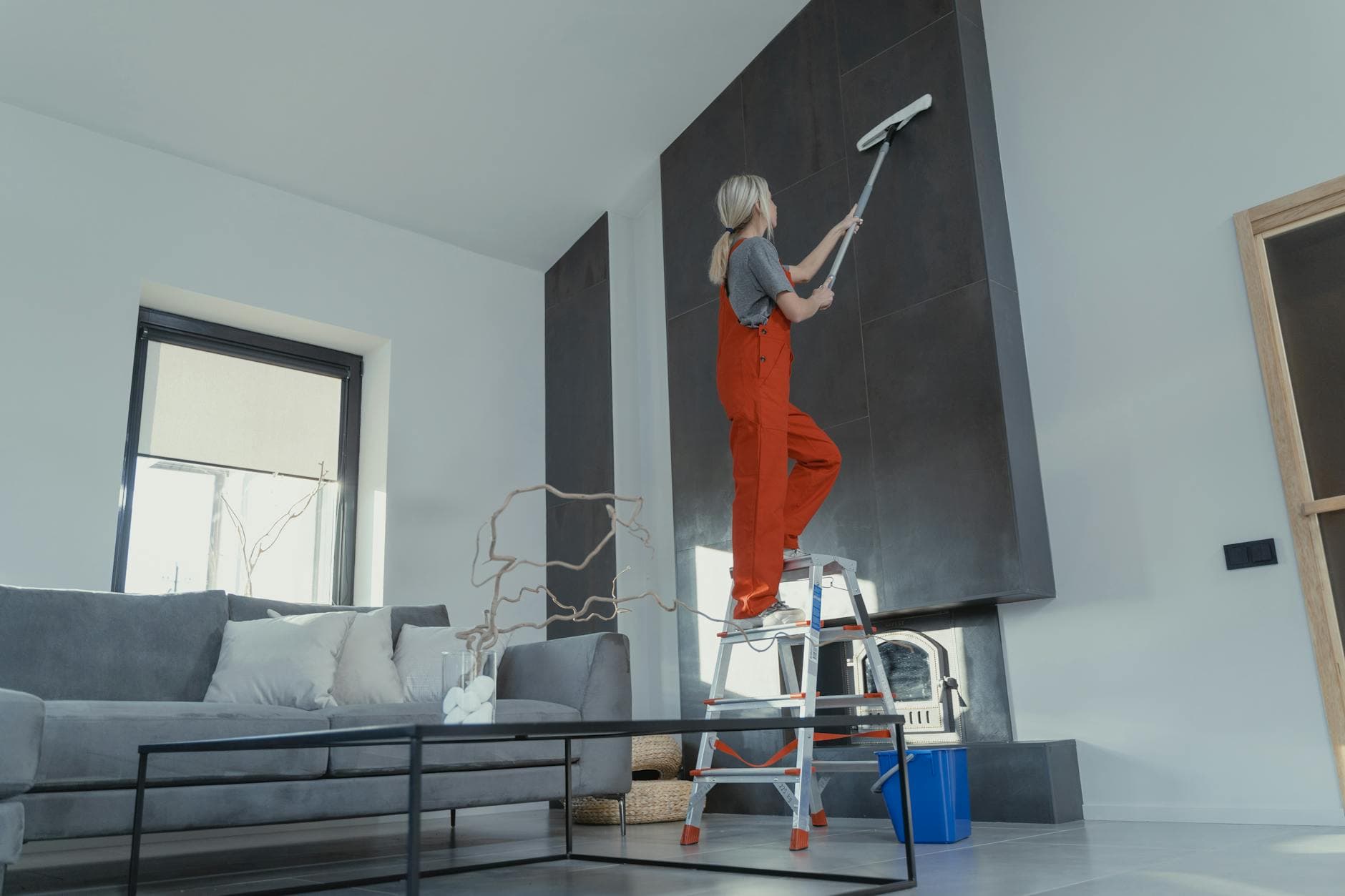 Your Business cleaner in red overalls on a ladder cleaning a high wall in a Manhattan apartment — Move-In/Move-Out Cleaning in DUMBO, Brooklyn