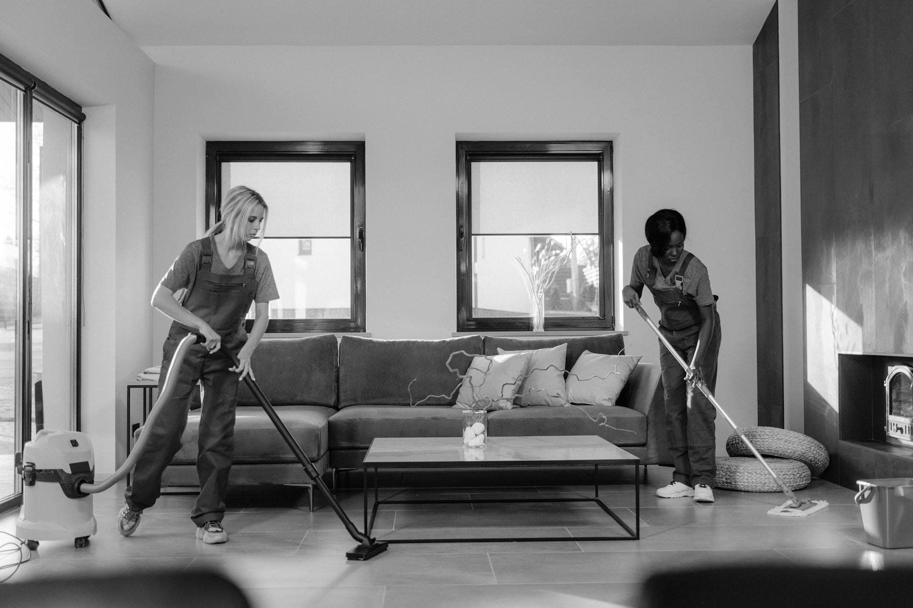 Two Your Business cleaners in work uniforms using a vacuum and mop in a modern Manhattan living room — Office Cleaning in Williamsburg, Brooklyn