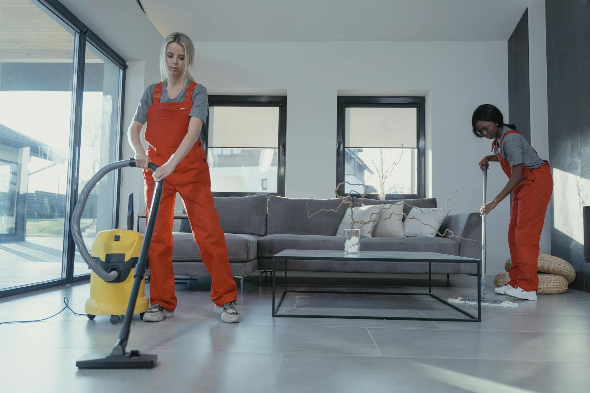 Two Your Business cleaners in red overalls vacuuming and sweeping a modern NYC living room — Office Cleaning in Elmhurst, Queens