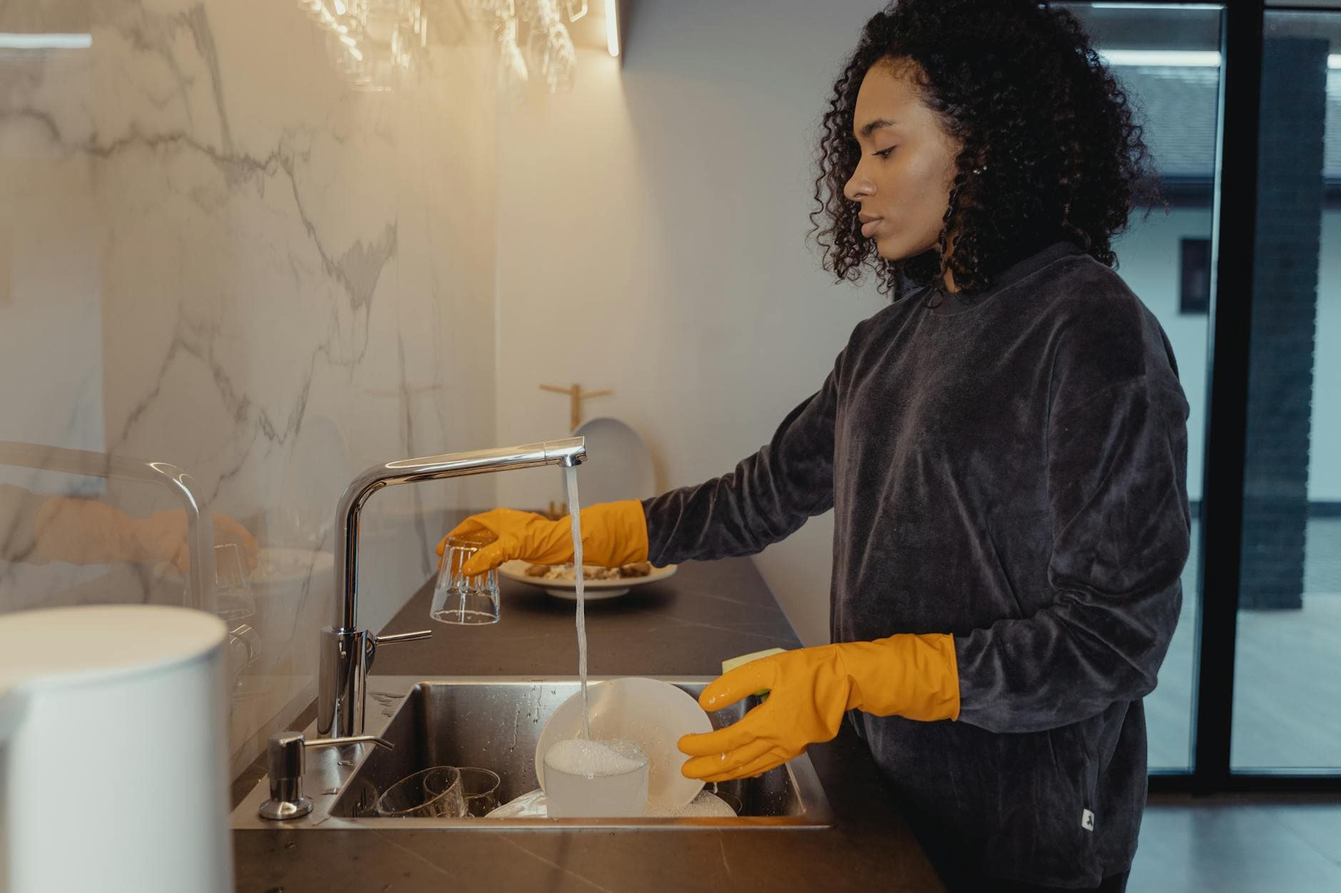 NYC maid wearing rubber gloves washing dishes in a modern Manhattan kitchen — Deep Cleaning in Albertson, Long Island
